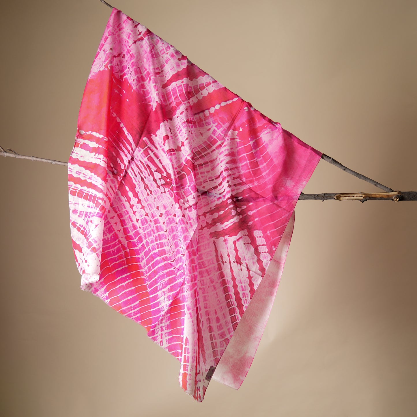 Pink and white patterned fabric draped over a branch against a beige background
