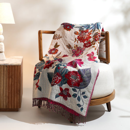 Floral patterned blanket draped over a wooden chair in a softly lit room.